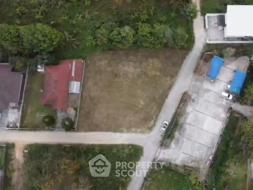 Aerial view of residential land plot with surrounding greenery and nearby houses.
