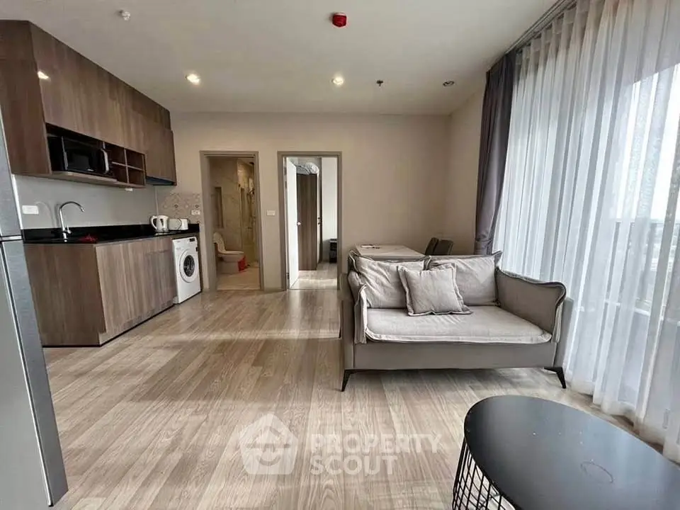 Modern open-plan living room with kitchen and dining area, featuring sleek wooden flooring and large windows.