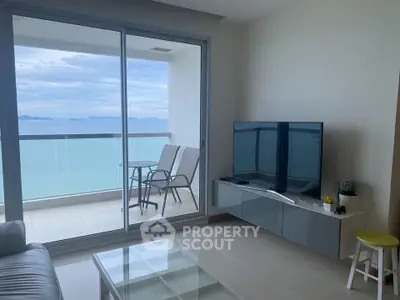 Modern living room with ocean view and balcony access, featuring sleek furniture and large TV.