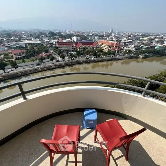 Stunning balcony view overlooking river and cityscape with red chairs for relaxation.