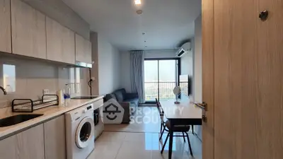 Modern apartment interior with open kitchen and living room, featuring a washing machine and city view.