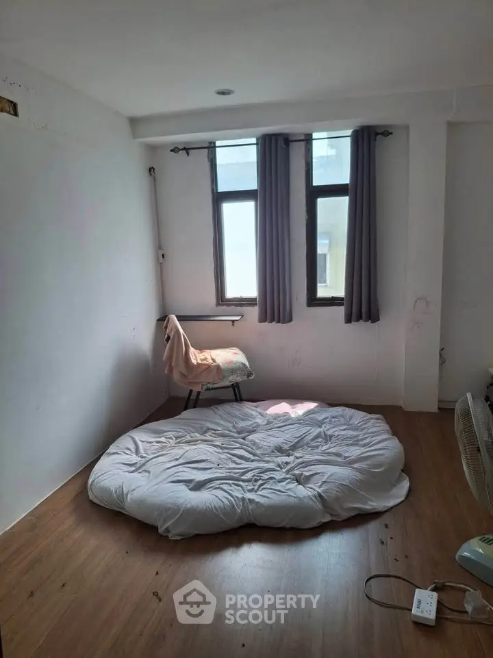 Minimalist bedroom with floor mattress and natural light from two windows.