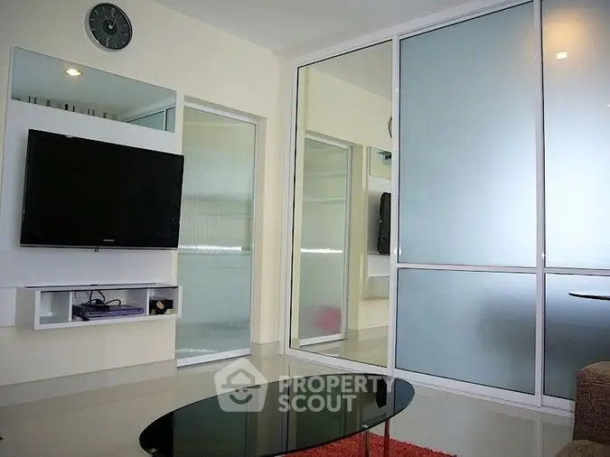 Modern living room with sleek glass table and wall-mounted TV, featuring stylish frosted glass sliding doors.