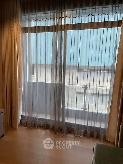 Spacious room with large window and sheer curtains offering natural light and urban view.