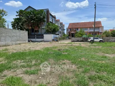 Vacant land plot with potential for development, surrounded by residential buildings under a clear blue sky.