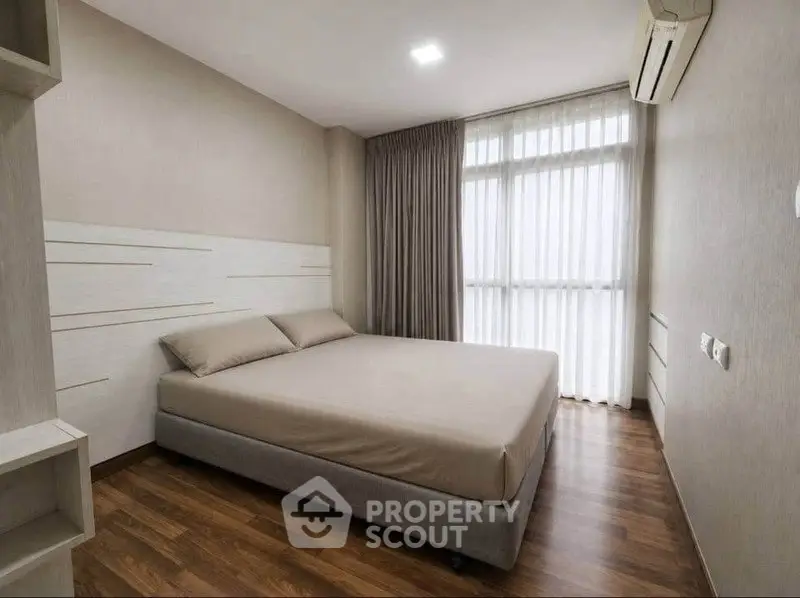 Modern minimalist bedroom with wooden flooring and large window for natural light.