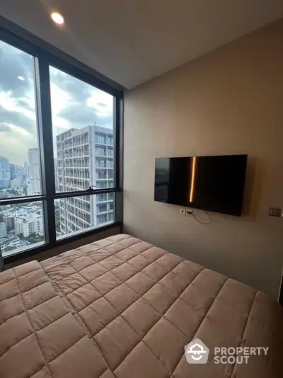 Modern bedroom with city view and wall-mounted TV in high-rise apartment.