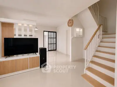 Modern living room with sleek staircase and large TV, featuring minimalist design and neutral tones.