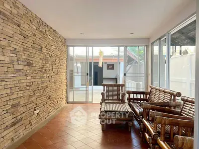 Charming sunlit room with rustic stone wall and bamboo furniture, perfect for relaxation.