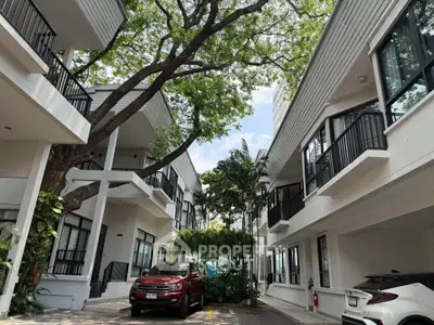 Modern townhouse complex with lush greenery and parked cars, showcasing contemporary architecture and serene environment.
