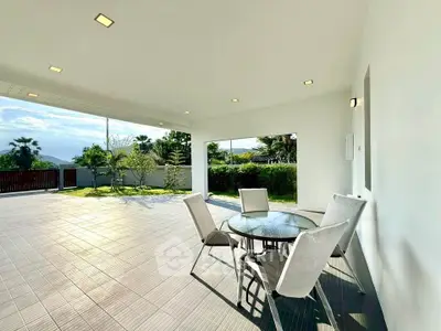 Spacious covered patio with outdoor seating and scenic garden view, perfect for relaxation and entertainment.