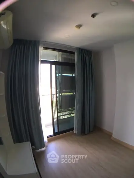 Bright room with sliding glass doors leading to a balcony, featuring elegant curtains and wooden flooring.