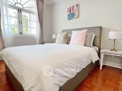 Elegant bedroom with large bed and stylish decor, featuring natural light through classic windows.
