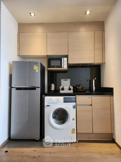 Modern compact kitchen with fridge, washing machine, and microwave in sleek wooden cabinetry.