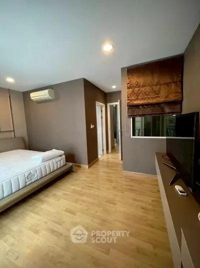 Spacious bedroom with modern decor and natural light, featuring a comfortable bed and sleek TV setup.