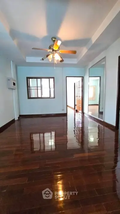 Spacious living room with polished wooden floors and ceiling fan in modern apartment.