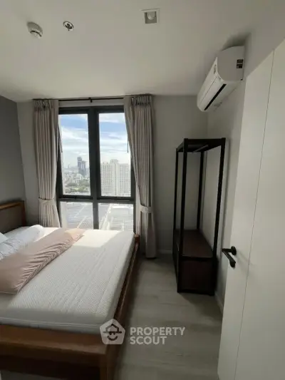 Modern bedroom with large window offering city view, featuring minimalist decor and air conditioning.