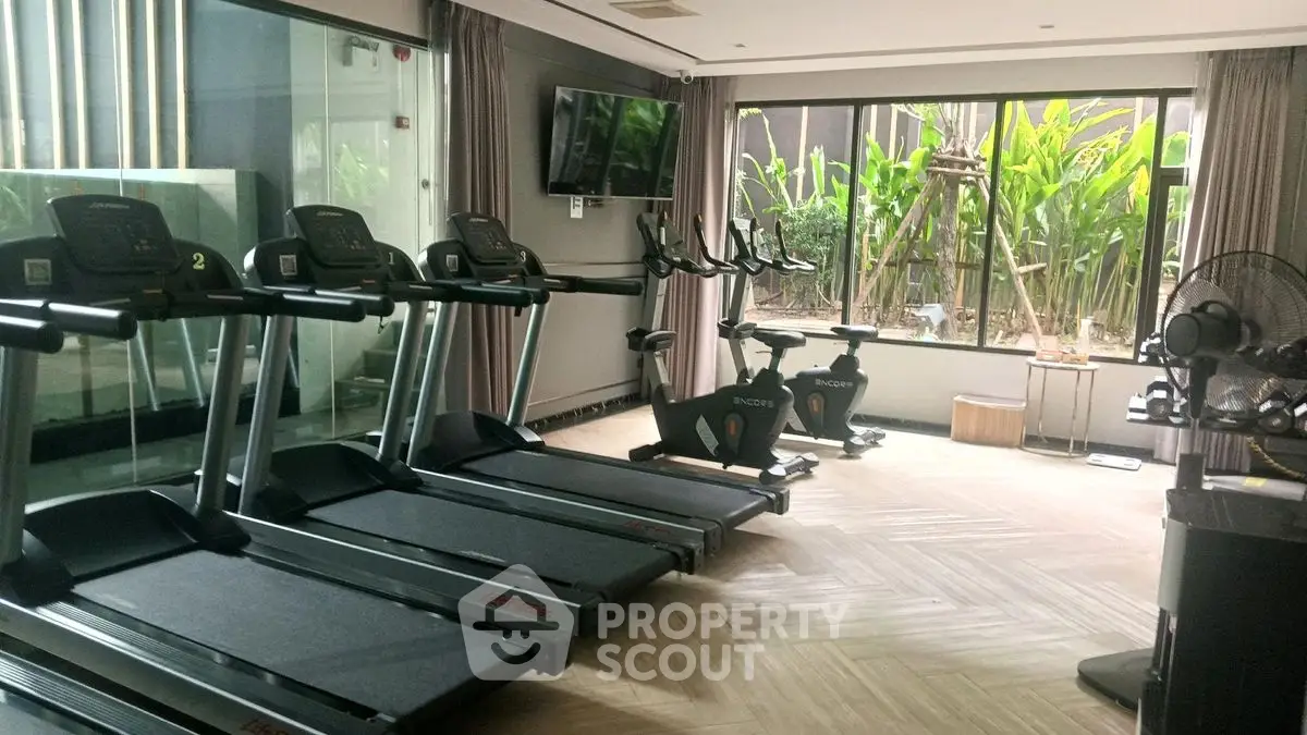 Modern gym with treadmills and exercise bikes overlooking a lush garden view.