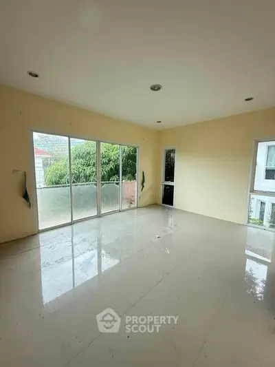 Spacious empty room with large windows and glossy tiled floor, offering abundant natural light and garden view.