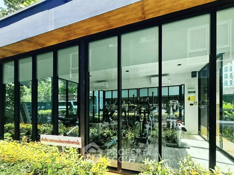 Modern gym with large glass windows and lush garden view in a residential building.