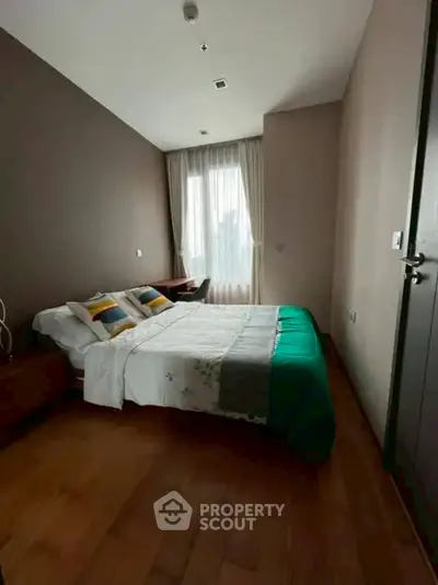 Cozy bedroom with wooden flooring and natural light through large window.