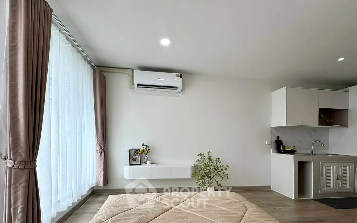 Modern bedroom with air conditioning and kitchenette, featuring large windows and elegant curtains.