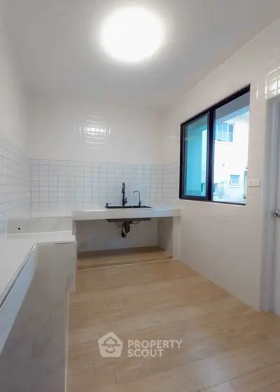 Spacious modern kitchen with sleek white tiles and large window for natural light.