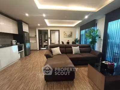 Spacious modern living room with open kitchen, featuring sleek furniture and large windows for natural light.
