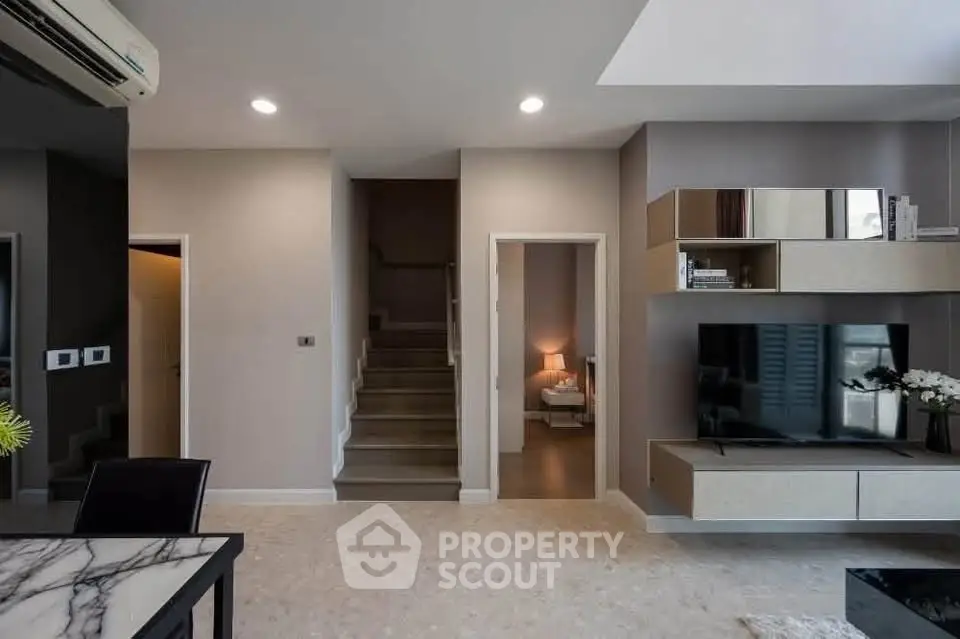 Modern living room with stylish decor and open layout, featuring a TV and elegant shelving.