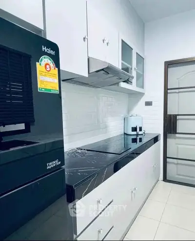Modern kitchen with sleek black and white design, featuring a Haier refrigerator and rice cooker.