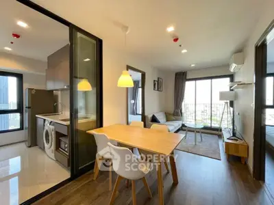 Modern open-plan living room with kitchen and dining area, featuring stylish furniture and large windows.
