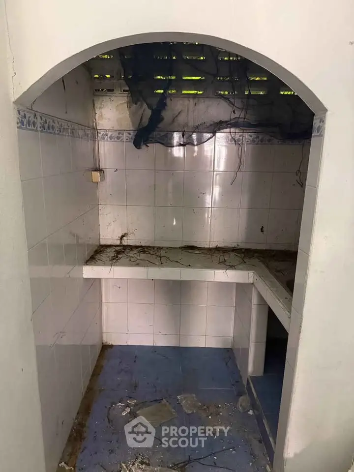 Charming fixer-upper kitchen space with tiled walls and arched entry, ready for renovation.