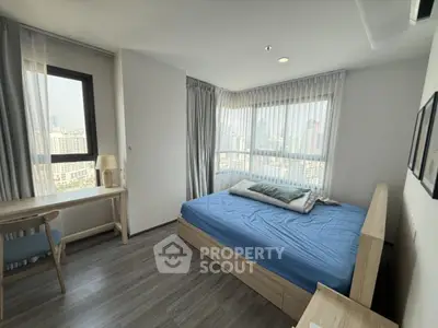 Modern bedroom with city view, featuring a cozy bed and study desk, perfect for urban living.