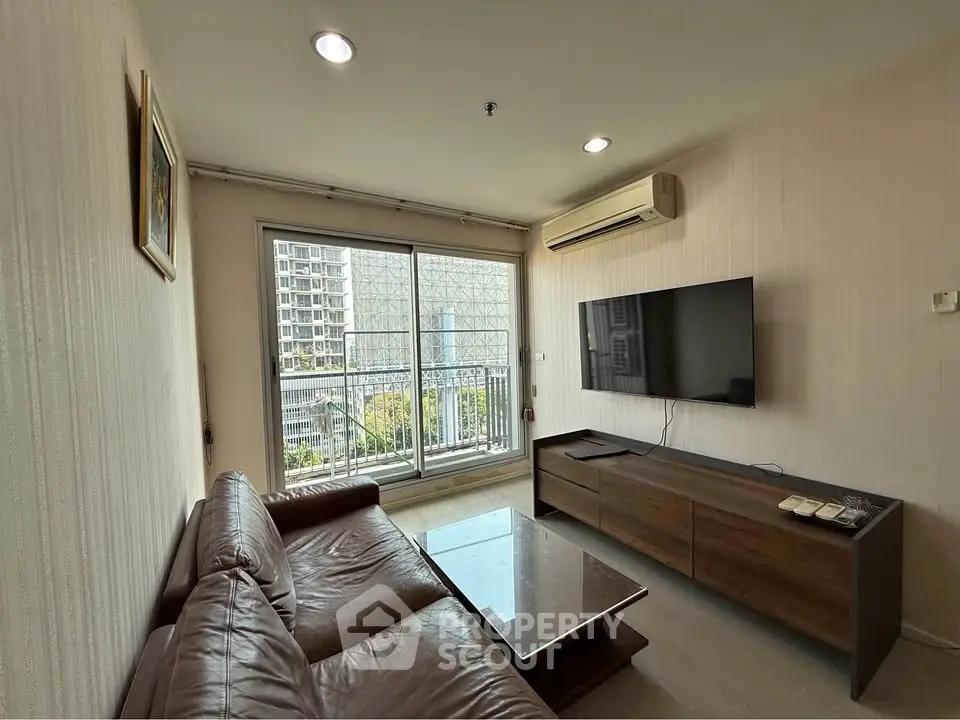 Modern living room with leather sofa, wall-mounted TV, and balcony view in urban apartment.