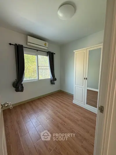 Spacious bedroom with wooden flooring and large window for natural light.