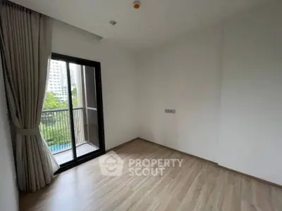 Spacious empty room with wooden flooring and balcony access in modern apartment.