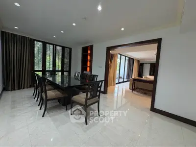 Spacious dining area with elegant table and chairs, adjacent to a bright living room with large windows.