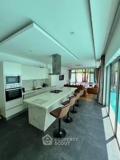 Luxurious open-layout kitchen with island and pool view, featuring modern appliances and stylish bar stools.