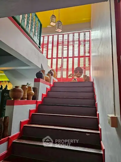Charming staircase with vibrant red accents and decorative pottery in a stylish home.