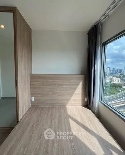 Modern bedroom with large window offering cityscape view and wooden flooring