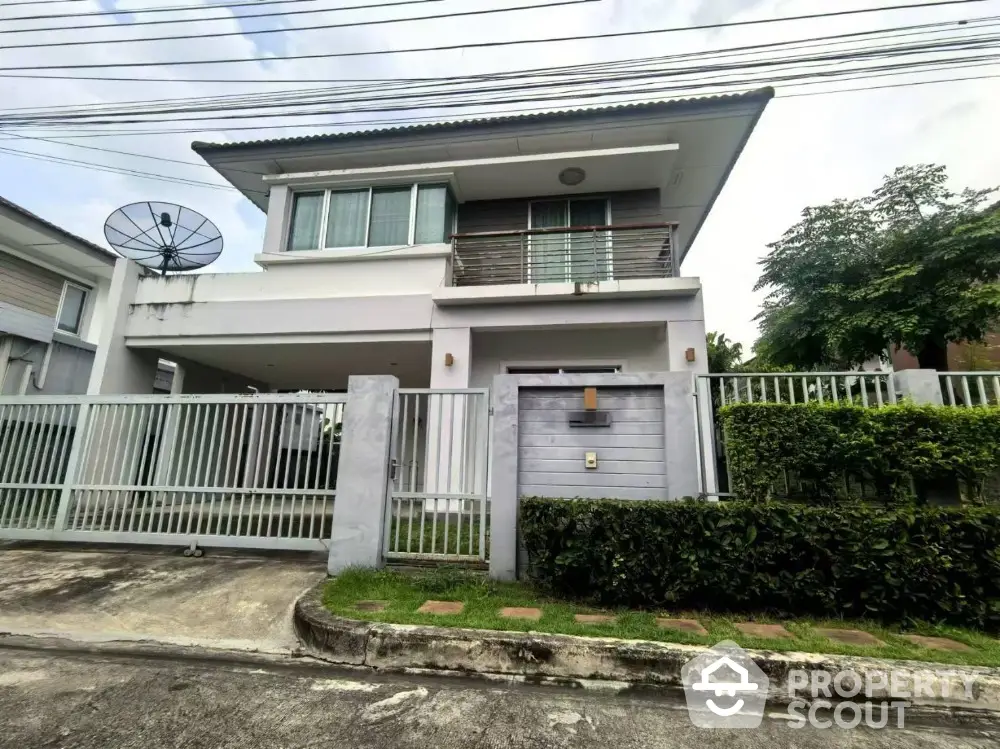 Modern two-story house with balcony and gated entrance in suburban neighborhood