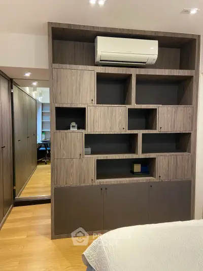 Modern bedroom with built-in wooden shelving and air conditioning unit, featuring sleek design and ample storage.