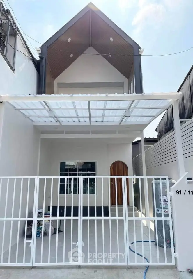 Modern two-story house with sleek design and gated entrance, featuring a spacious carport and contemporary architecture.