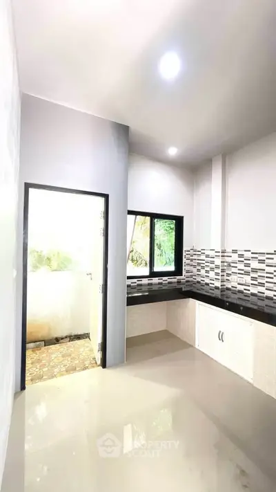 Modern kitchen with sleek countertops and stylish backsplash, featuring ample natural light and outdoor access.