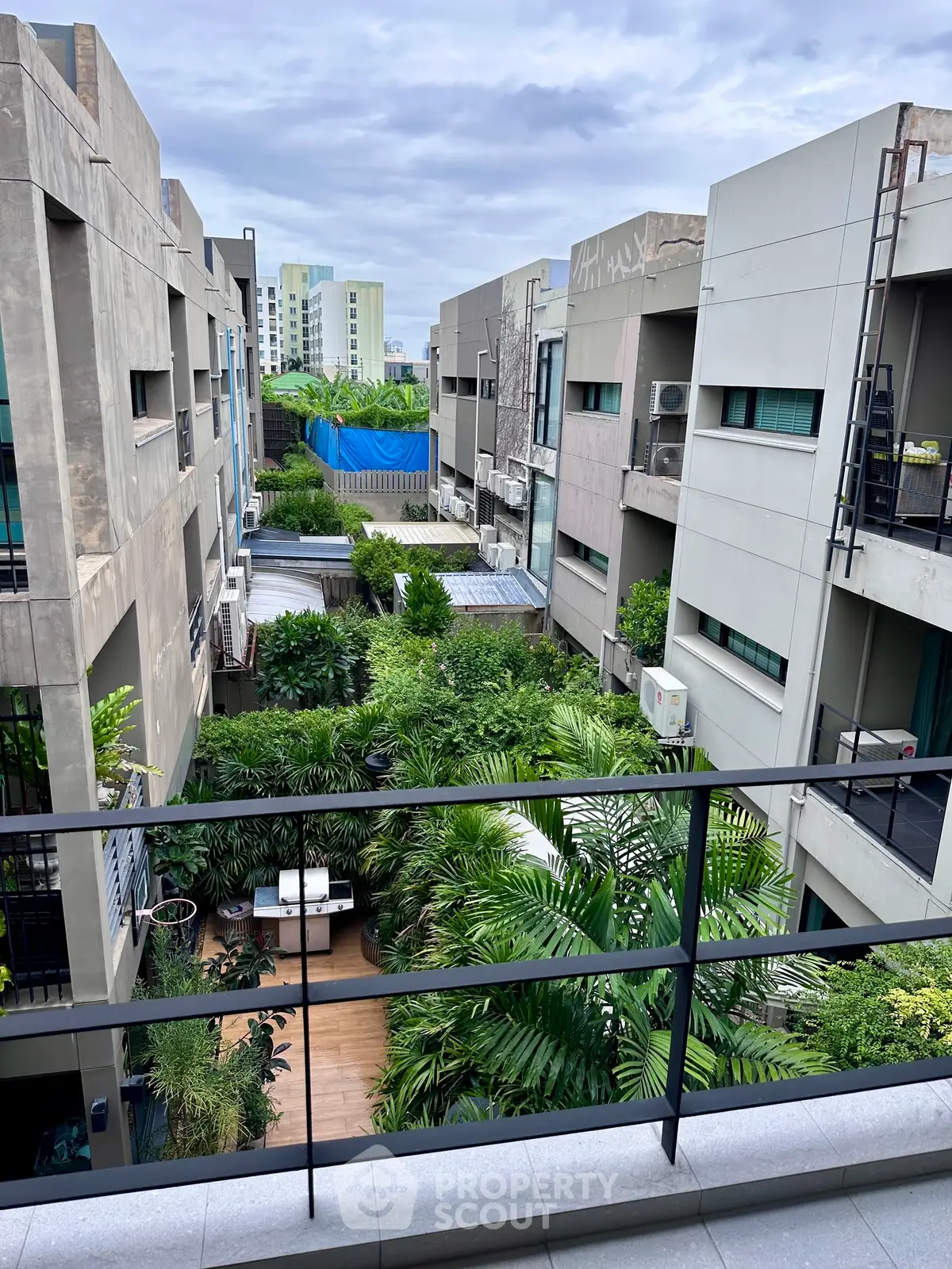 Modern urban apartment buildings with lush green garden view from balcony.