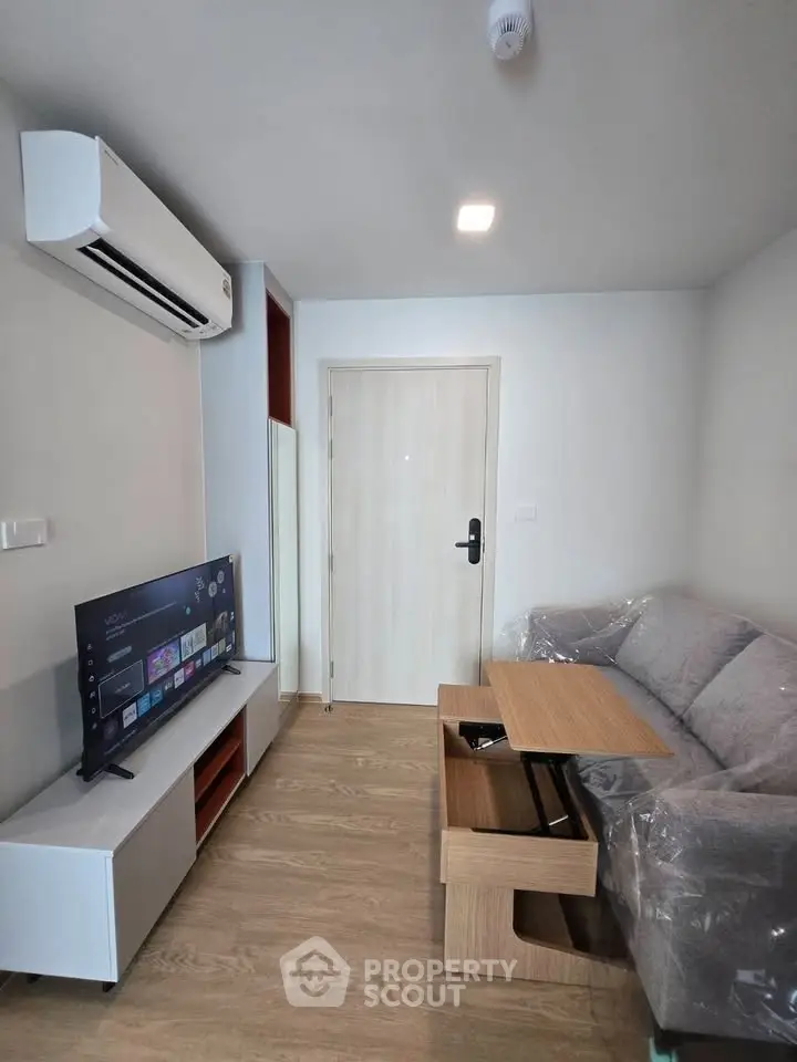 Modern living room with sleek furniture and wall-mounted TV, featuring a cozy sofa and air conditioning.