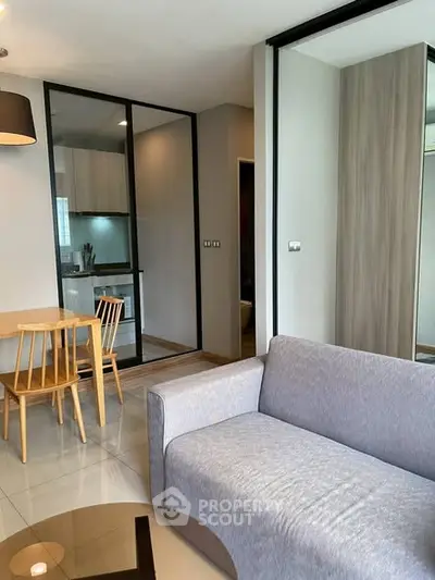 Modern living room with sleek furniture and glass partition leading to a compact kitchen.