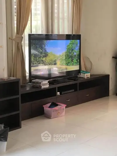 Spacious living room with modern TV setup and natural light through large windows.