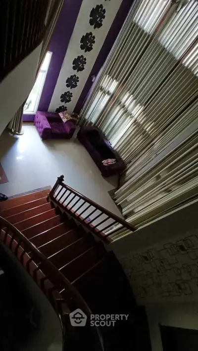 Elegant living room with high ceilings, stylish purple accents, and a wooden staircase, perfect for modern living.