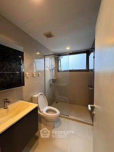 Modern bathroom with sleek fixtures and glass shower enclosure in contemporary apartment.
